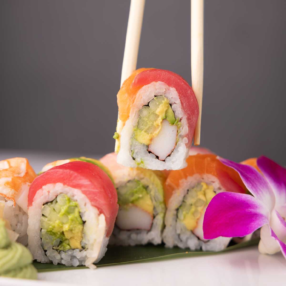 A rainbow sushi roll held with chopsticks, showcasing the artistry and taste of Sushi Albuquerque or Sushi Rio Rancho.